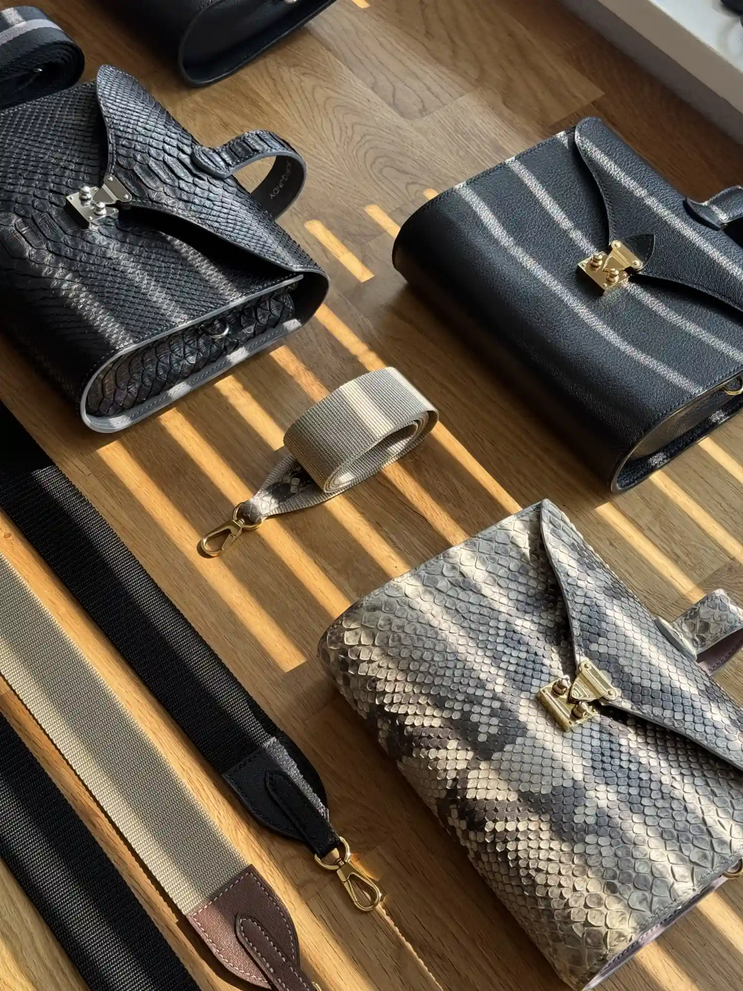 Maßgefertigte Taschen aus schwarzem Leder und geschuppter Haut mit gewebten Riemen auf einem Holzboden.