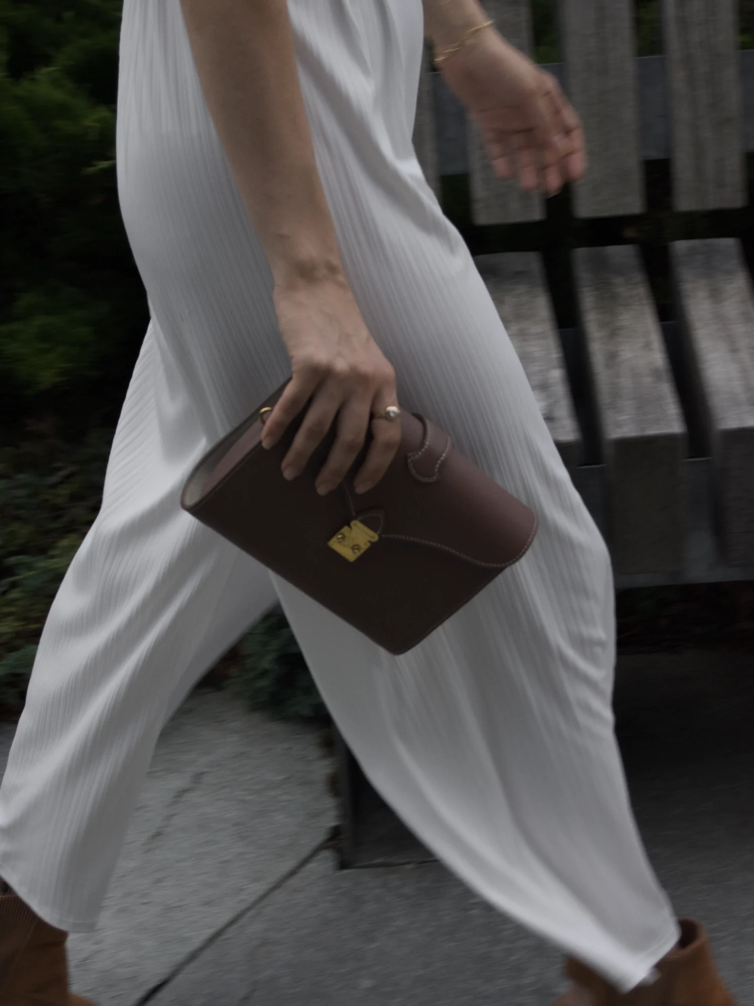 Femme en mouvement, sac Éclat marron tenu à la main, chaîne dorée en balancement